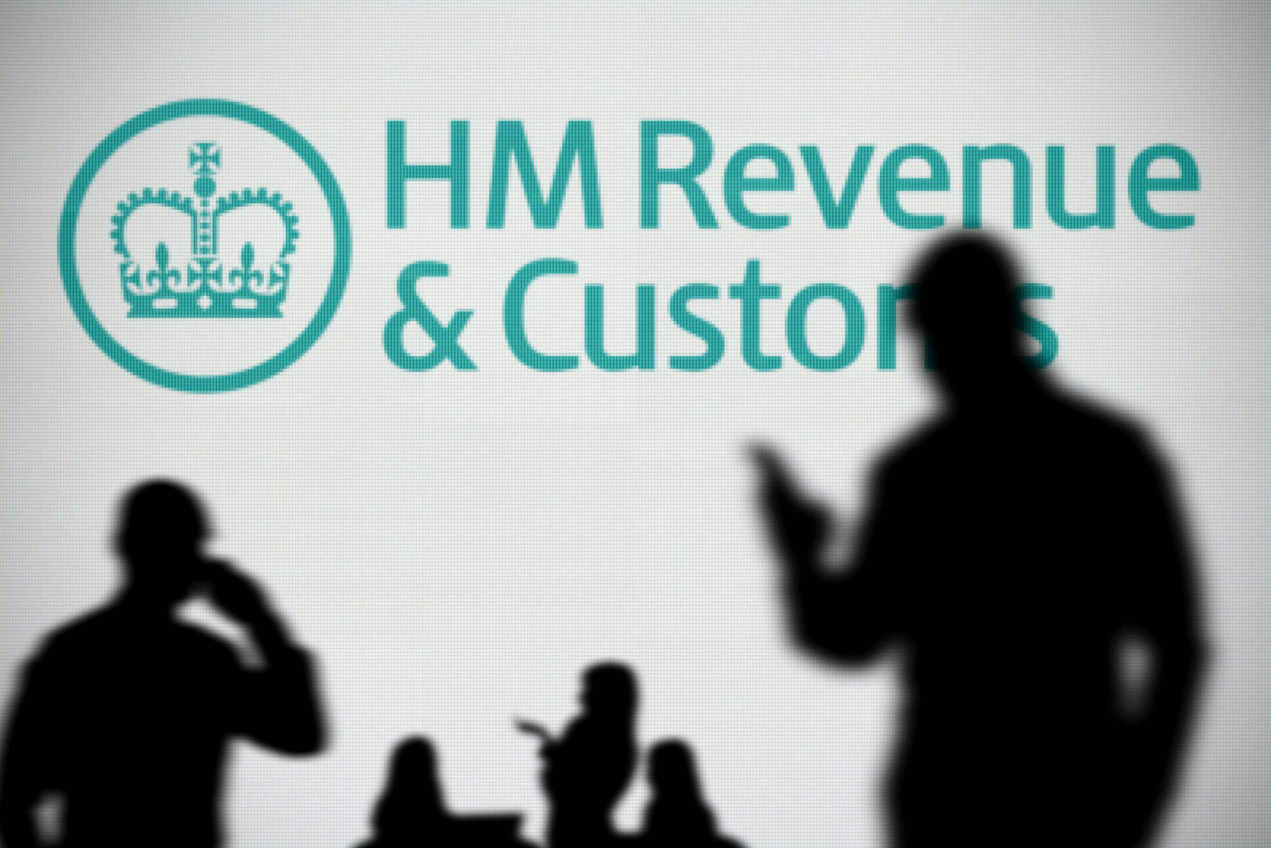 TCNMTR The HMRC logo is seen on an LED screen in the background while a silhouetted person uses a smartphone in the foreground (Editorial use only)
